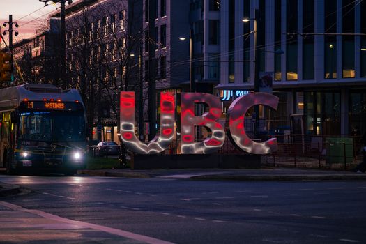 Evening scene of UBC sign illuminated with city bus at University Endowment Lands in Vancouver, BC.