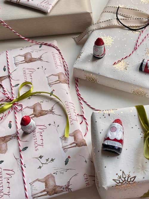 Free Festive Christmas gift wrapping with reindeer paper, ribbons, and Santa chocolates. Stock Photo