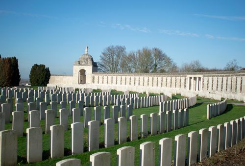 Free Serene World War I cemetery with aligned gravestones and a memorial building under a clear blue sky. Stock Photo