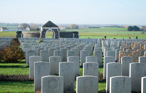Free Rows of stone graves in a military cemetery with a stone archway and rural backdrop. Stock Photo