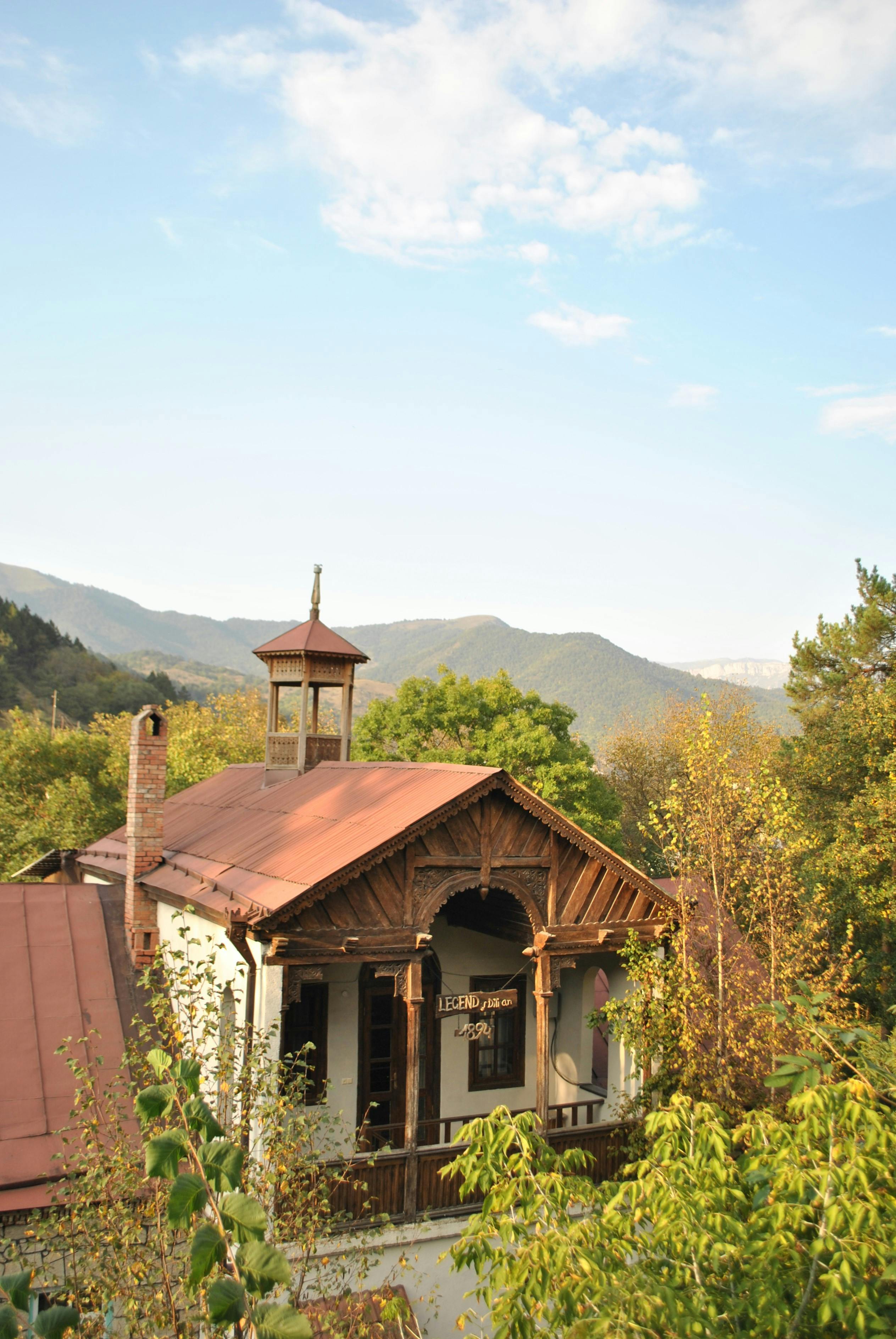 A picturesque mountain cottage surrounded by lush foliage under a bright sky.