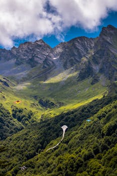 A vibrant scene from the Pyrenees in Occitanie, France with kites flying over lush green valleys.