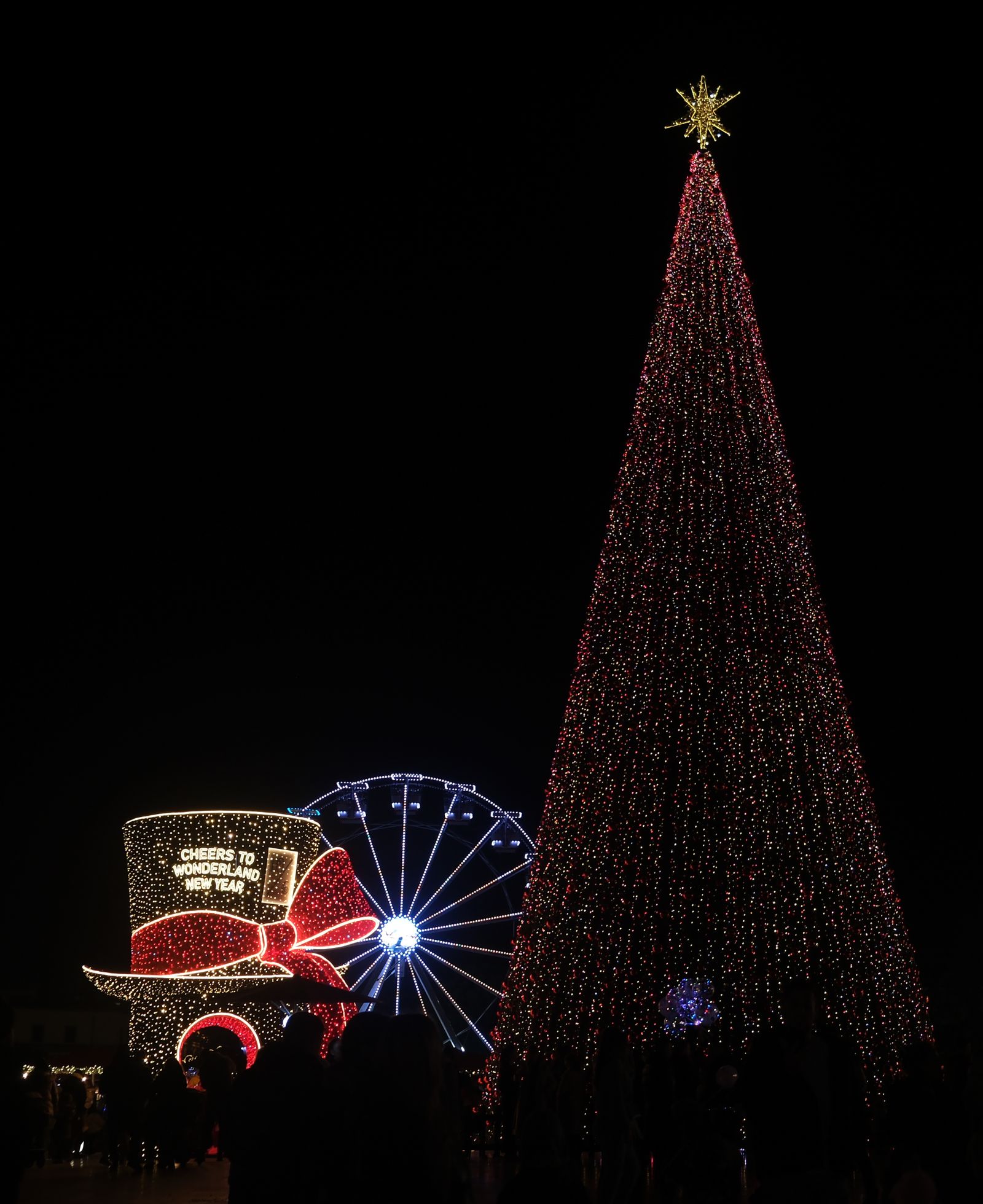 Sapin de Noël illuminé, grande roue et décorations festives la nuit à Tirana