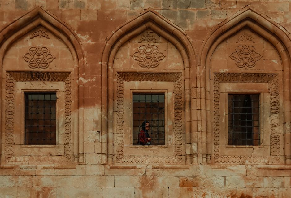 Woman standing at ornate stone window of historic building facade.