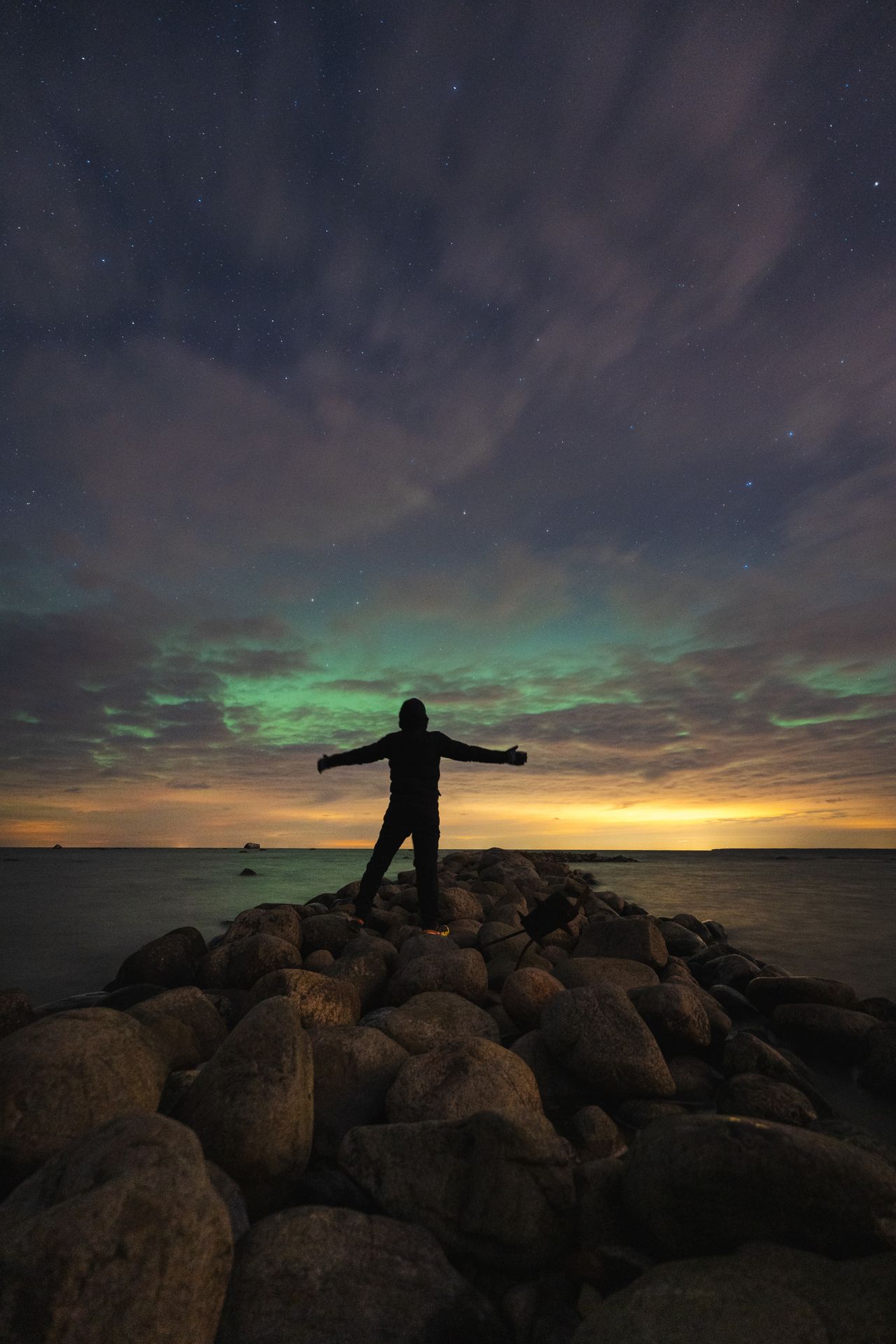 Person standing on rocks under green aurora borealis