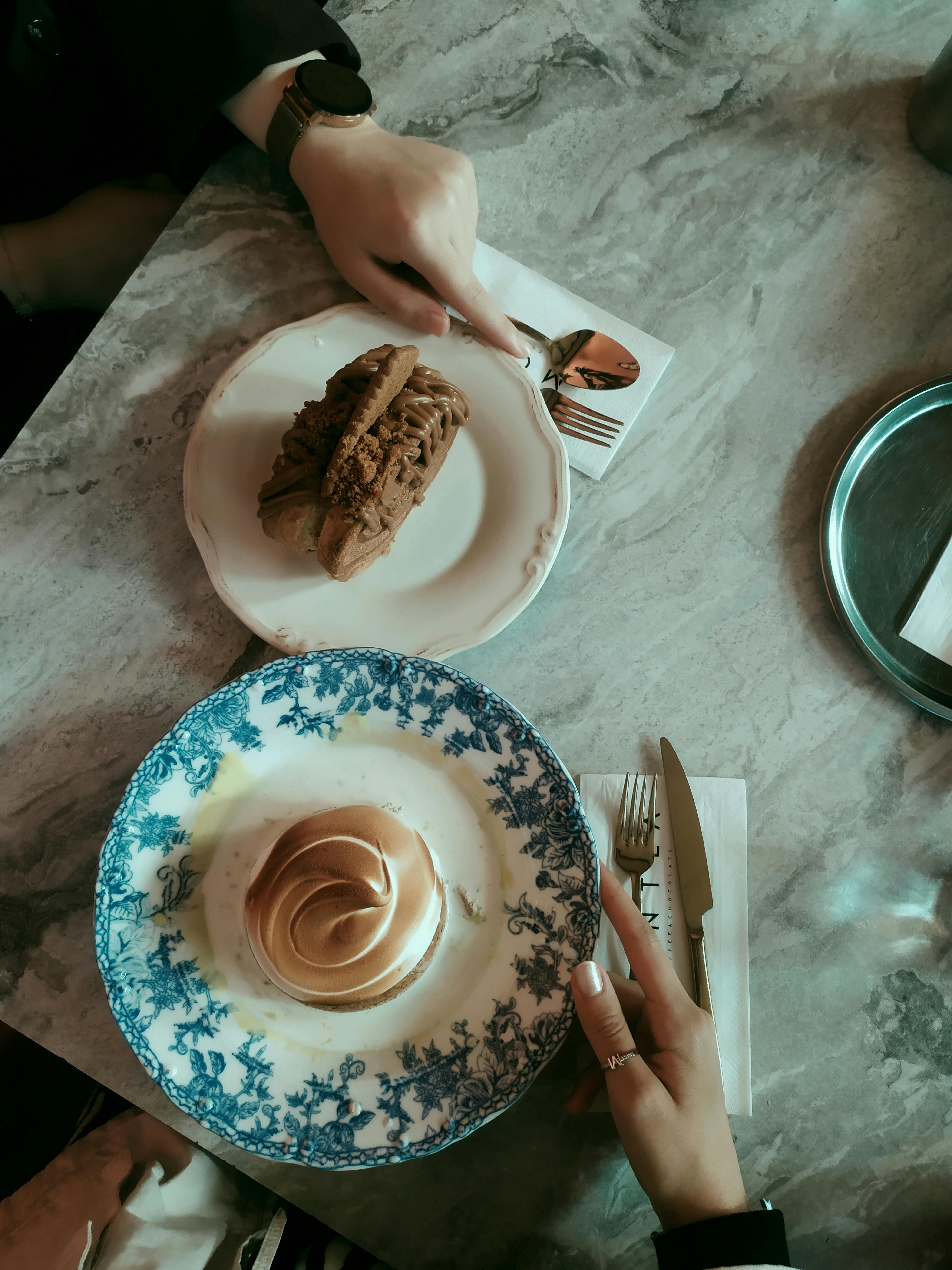 Top view of elegant desserts on a cafe table with two people reaching for them.