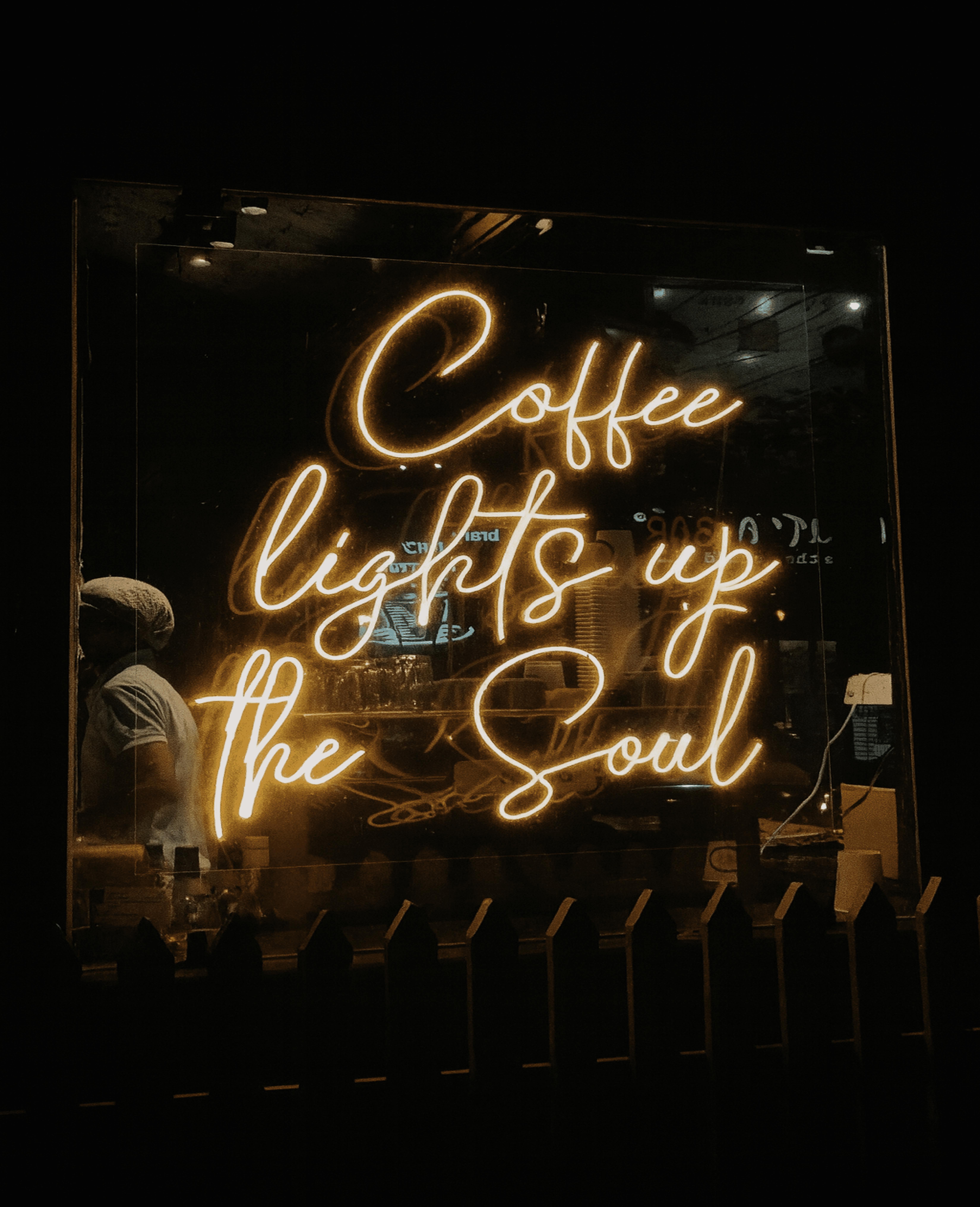무료 밤에 커피숍 창문에 '커피는 영혼을 밝혀준다'라는 문구가 적힌 따뜻한 네온사인이 걸려 있다. 스톡 사진
