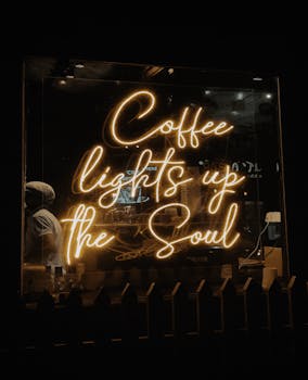 Warm neon sign with quote 'Coffee lights up the Soul' in a coffee shop window at night.