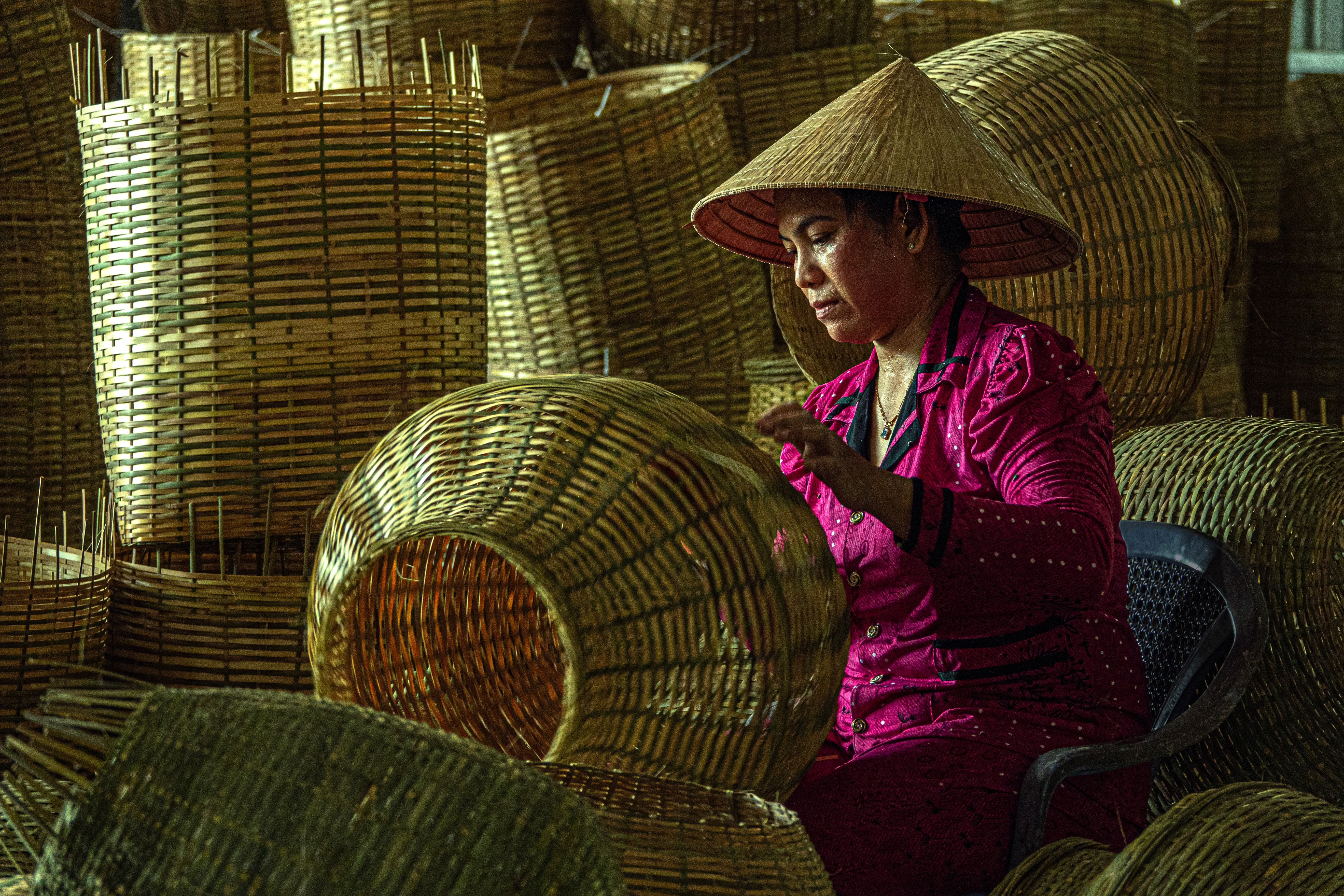 A woman in traditional attire skillfully weaving bamboo baskets indoors.