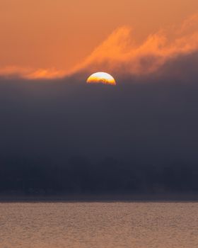 Serene sunset with sun partially hidden by clouds over a peaceful ocean.