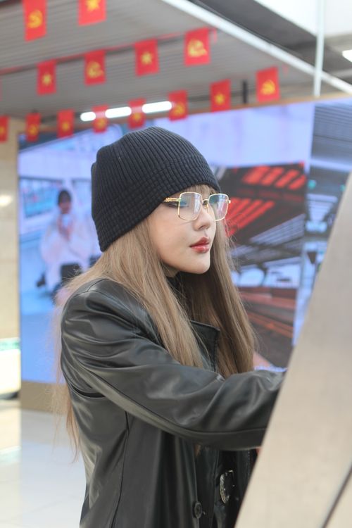 Free Woman in beanie and glasses using an ATM indoors decorated with flags. Stock Photo