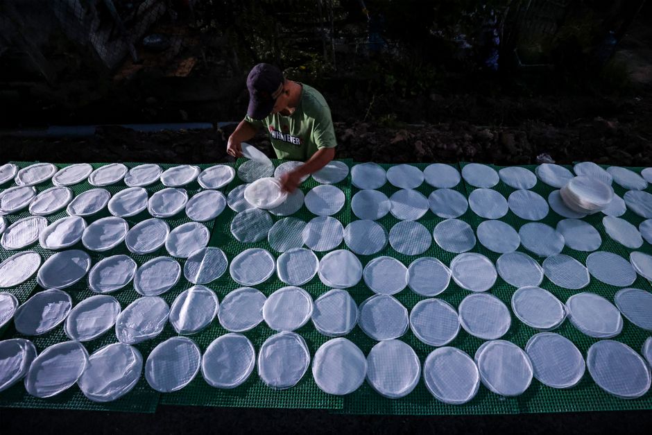 A person carefully arranges rice papers on a mat for drying under sunlight.