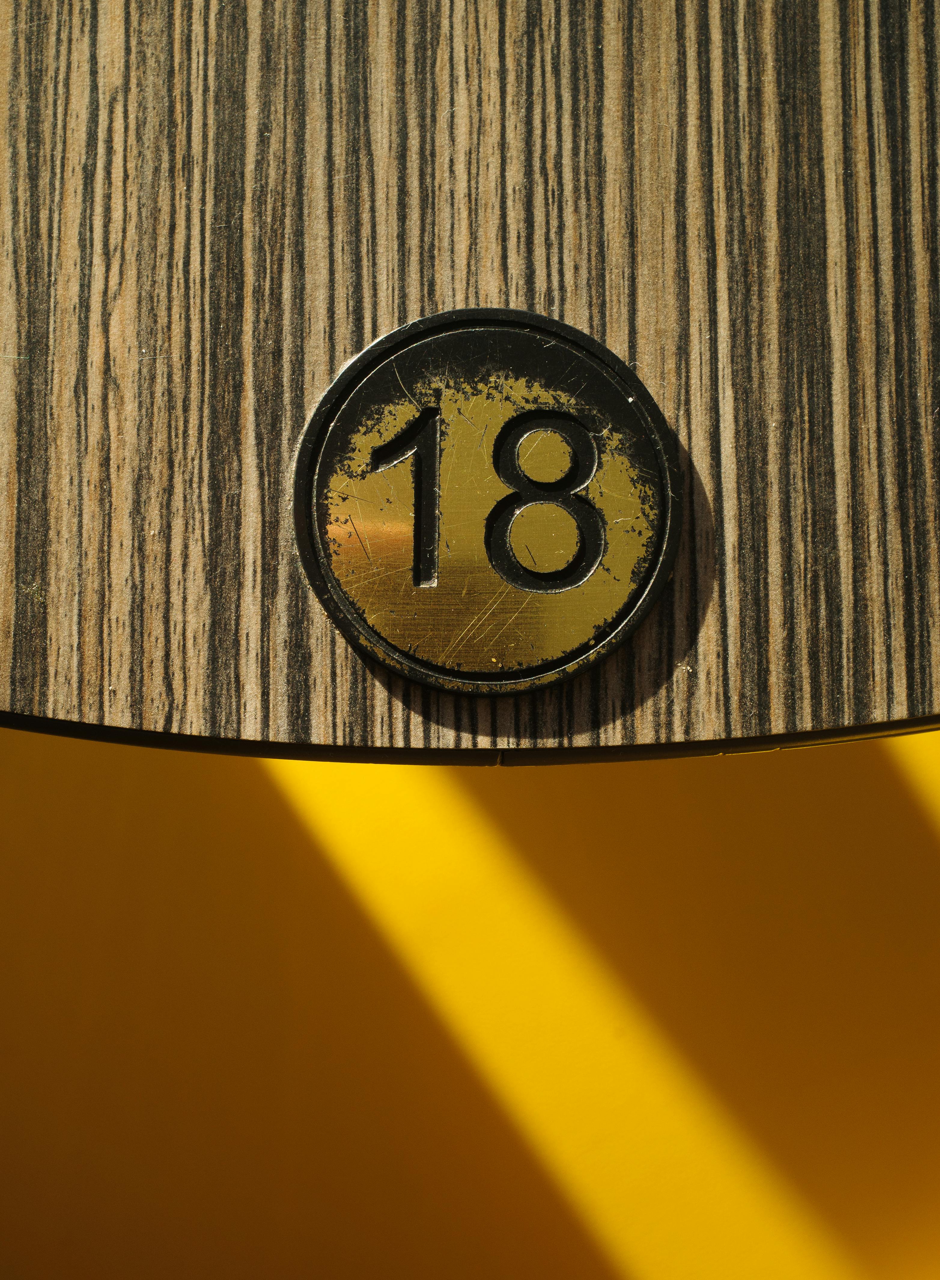 gratis Detailopname van nummer 18 op een houten paneel met een opvallende gele achtergrond en een schaduw. Stockfoto
