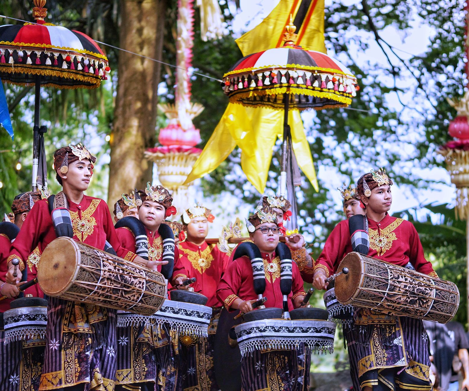 Balinese musicians in traditional attire perform energetically in a vibrant parade setting.