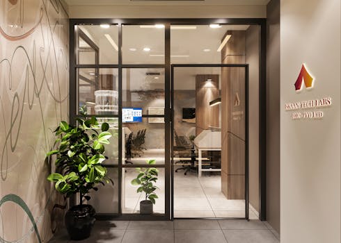 Stylish office entrance with glass door and company signage, featuring elegant decor and indoor plants.