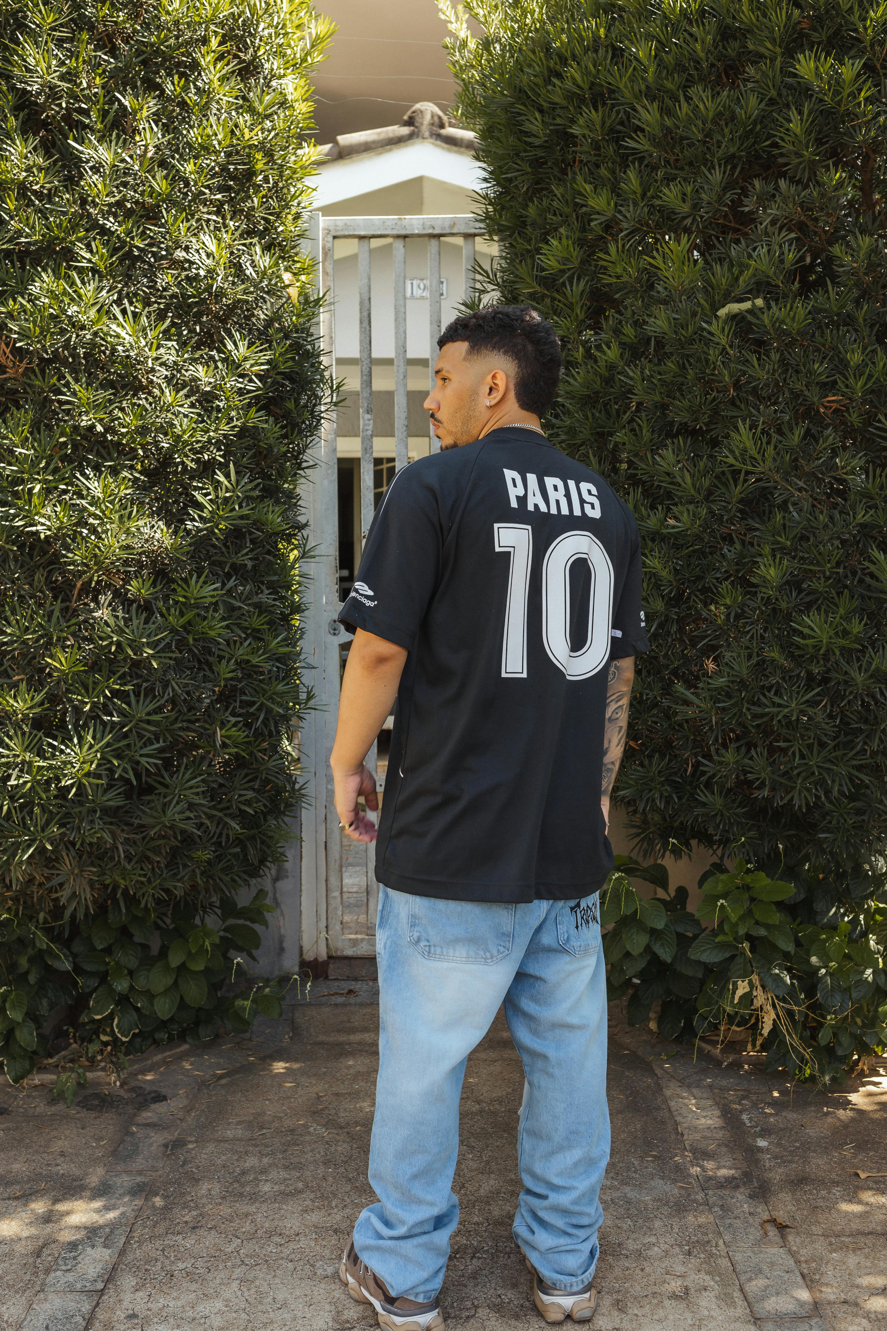Young man in casual streetwear stands outdoors by greenery in Presidente Prudente, Brazil.