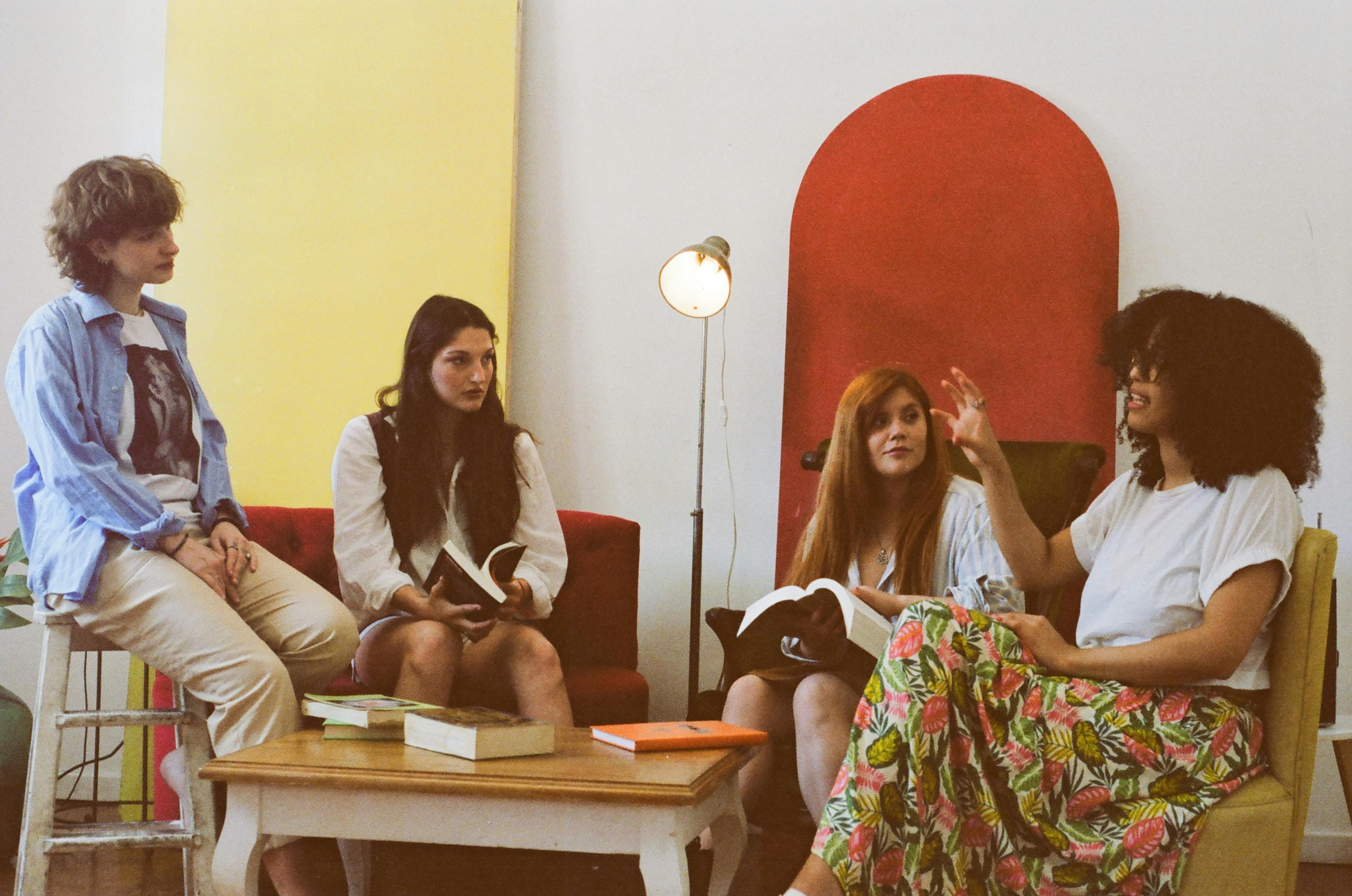 Kostnadsfria En grupp på fyra kvinnor diskuterar böcker i ett mysigt, färgglatt rum. Stock foto