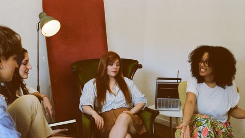 Four adults engaged in a relaxed group discussion in a cozy indoor space.