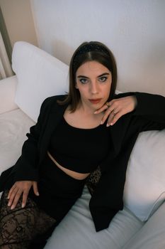 Stylish woman in black attire relaxing on a white sofa, exuding elegance and sophistication.