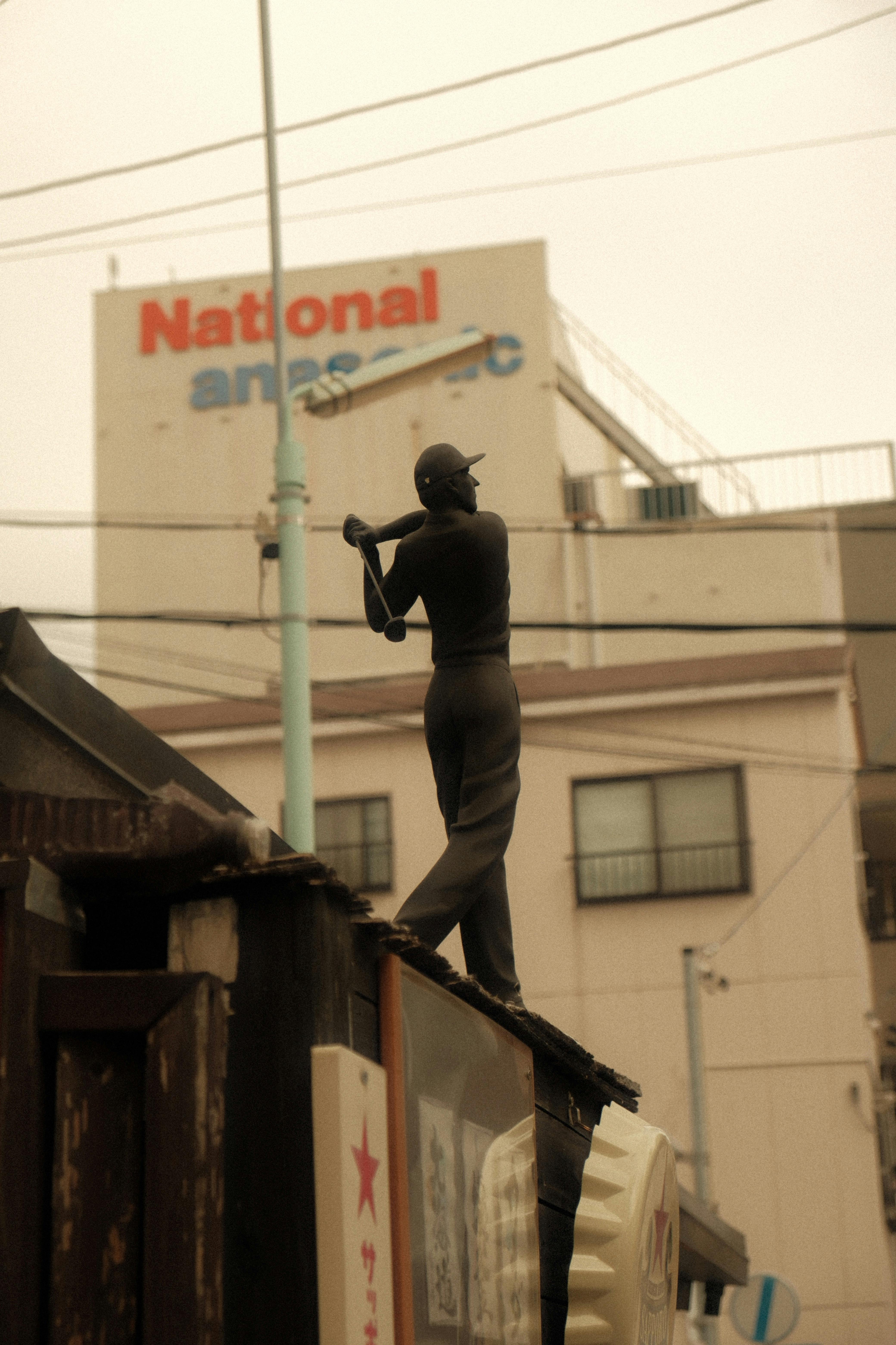 Statue of a golfer in front of a vintage advertising sign in an urban setting.
