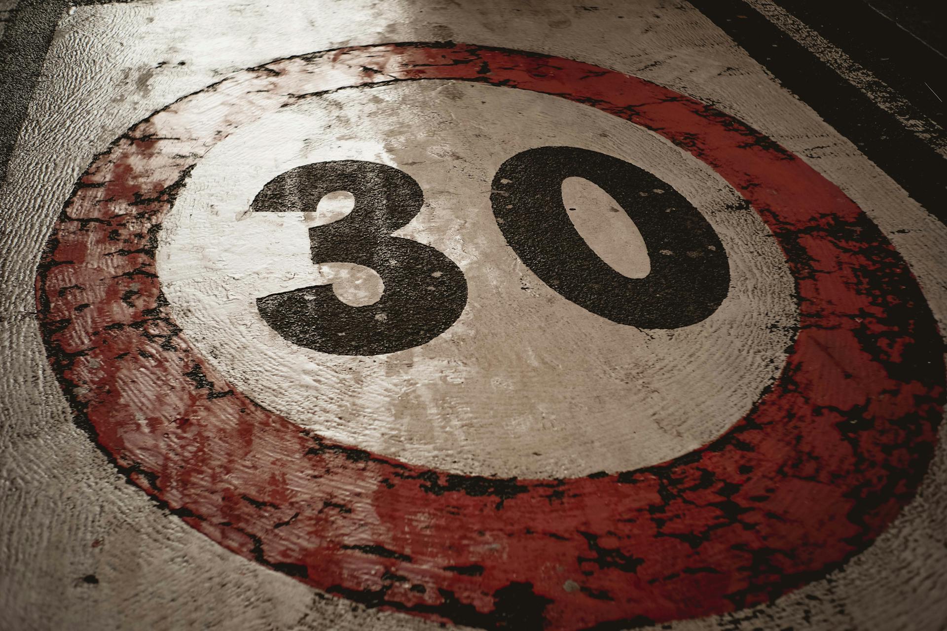 A weathered 30 speed limit sign painted on an asphalt road surface.