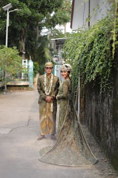 Indonesian couple in traditional wedding dress outdoors, full-length view.
