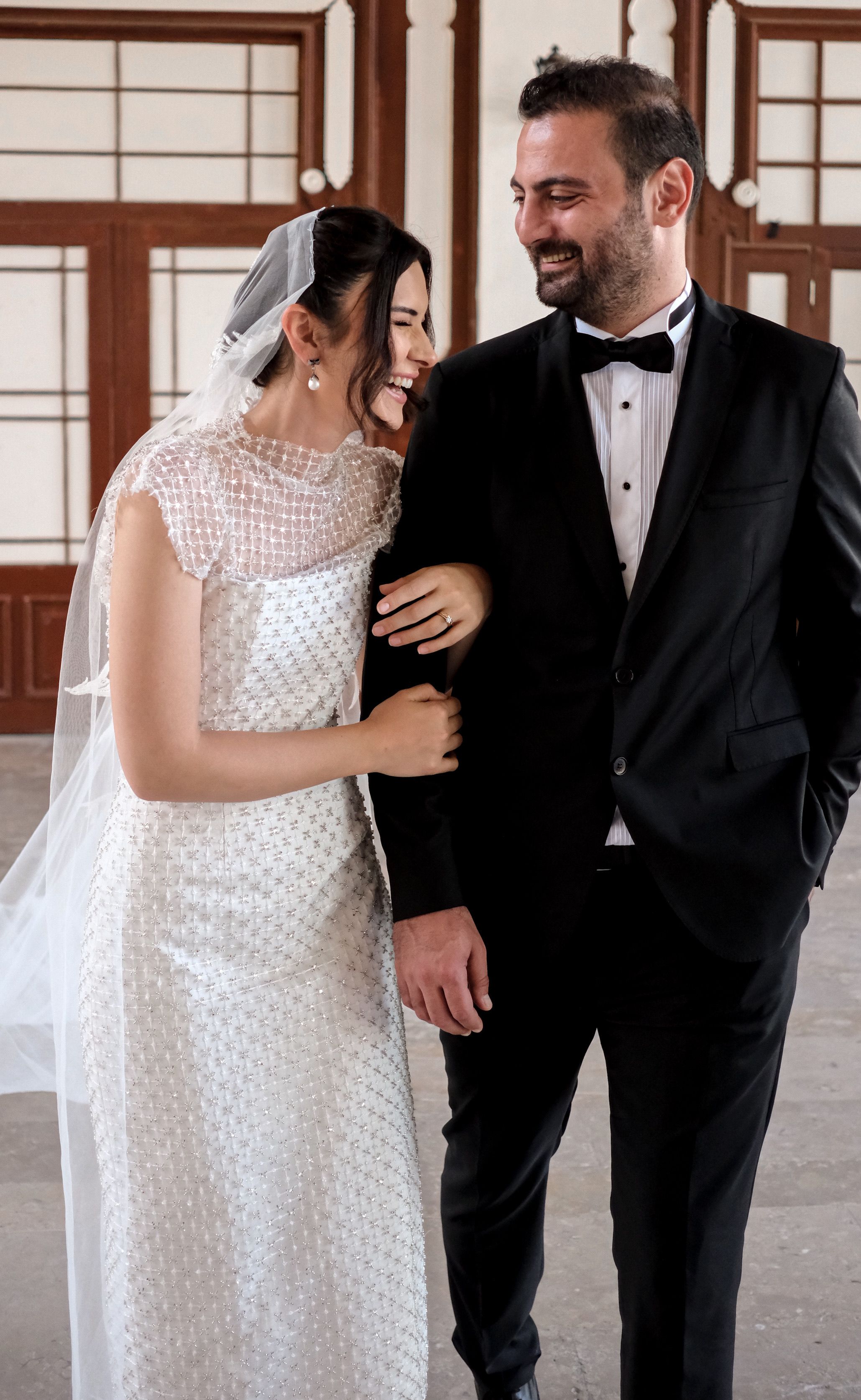 A bride and groom share a joyful moment indoors, dressed in elegant wedding attire.