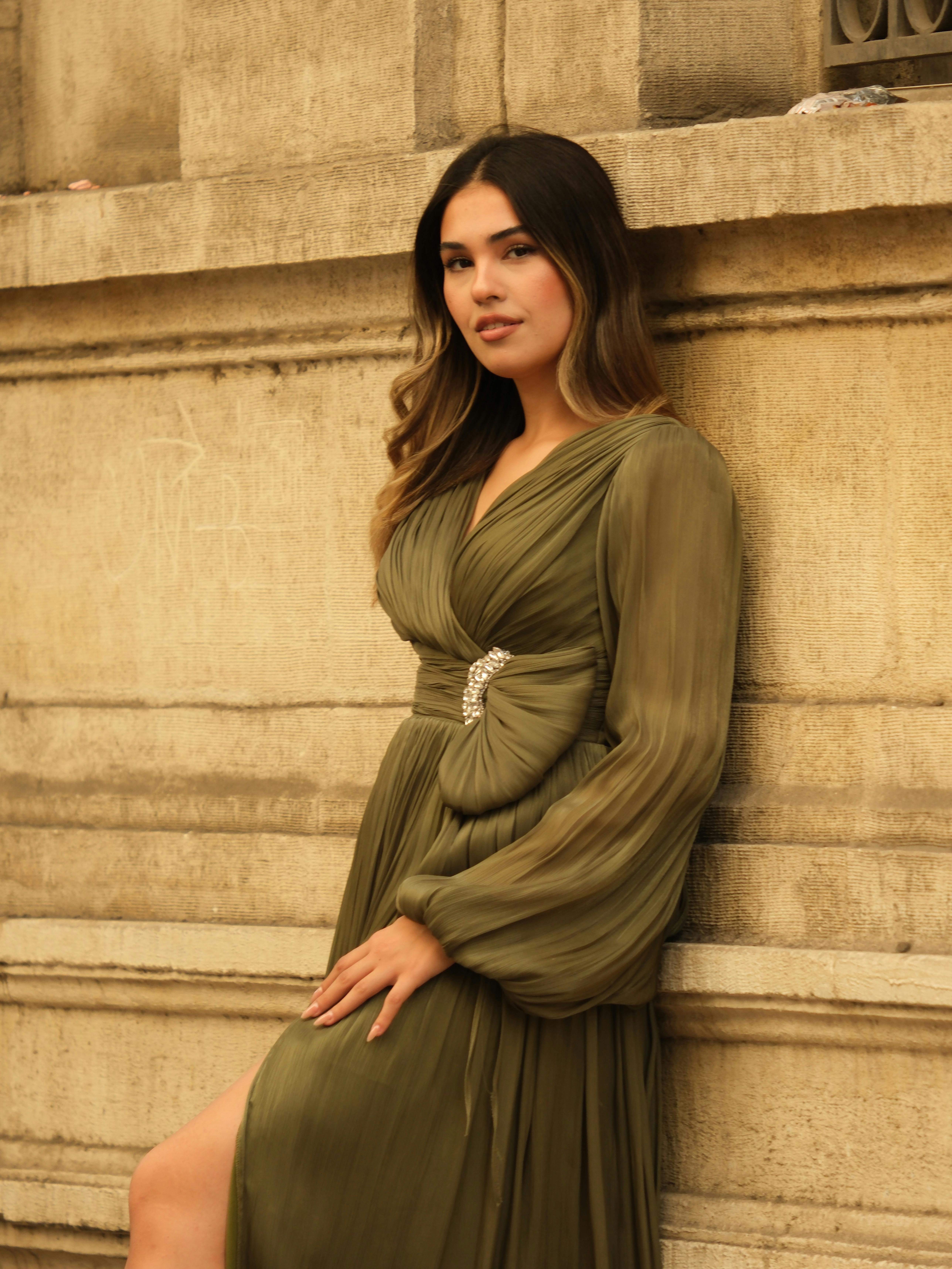 Woman leaning against a stone wall in an elegant green dress, exuding confidence and poise.