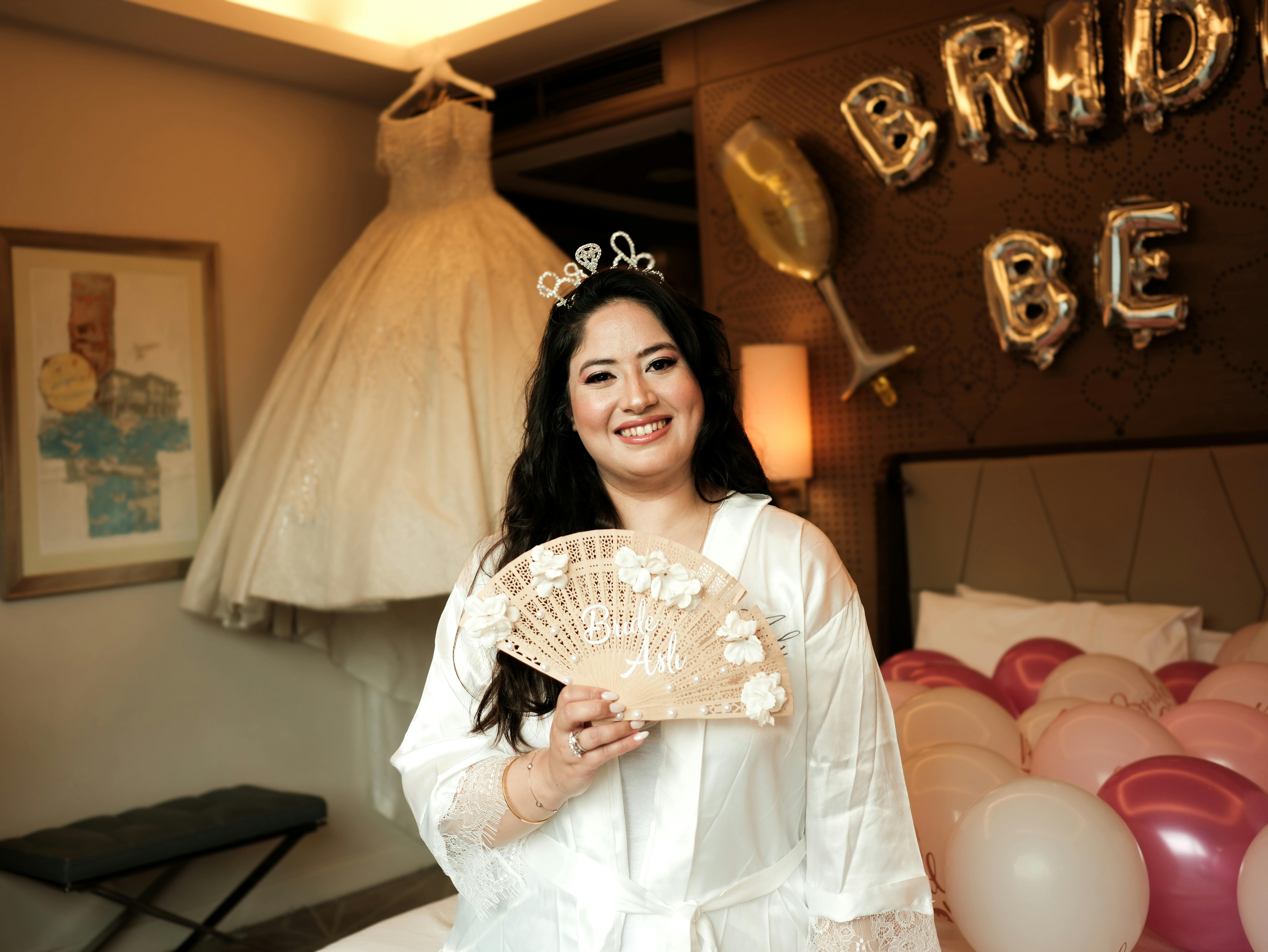 Bride smiling in a hotel room with gown, balloons, and 'Bride to Be' decor.