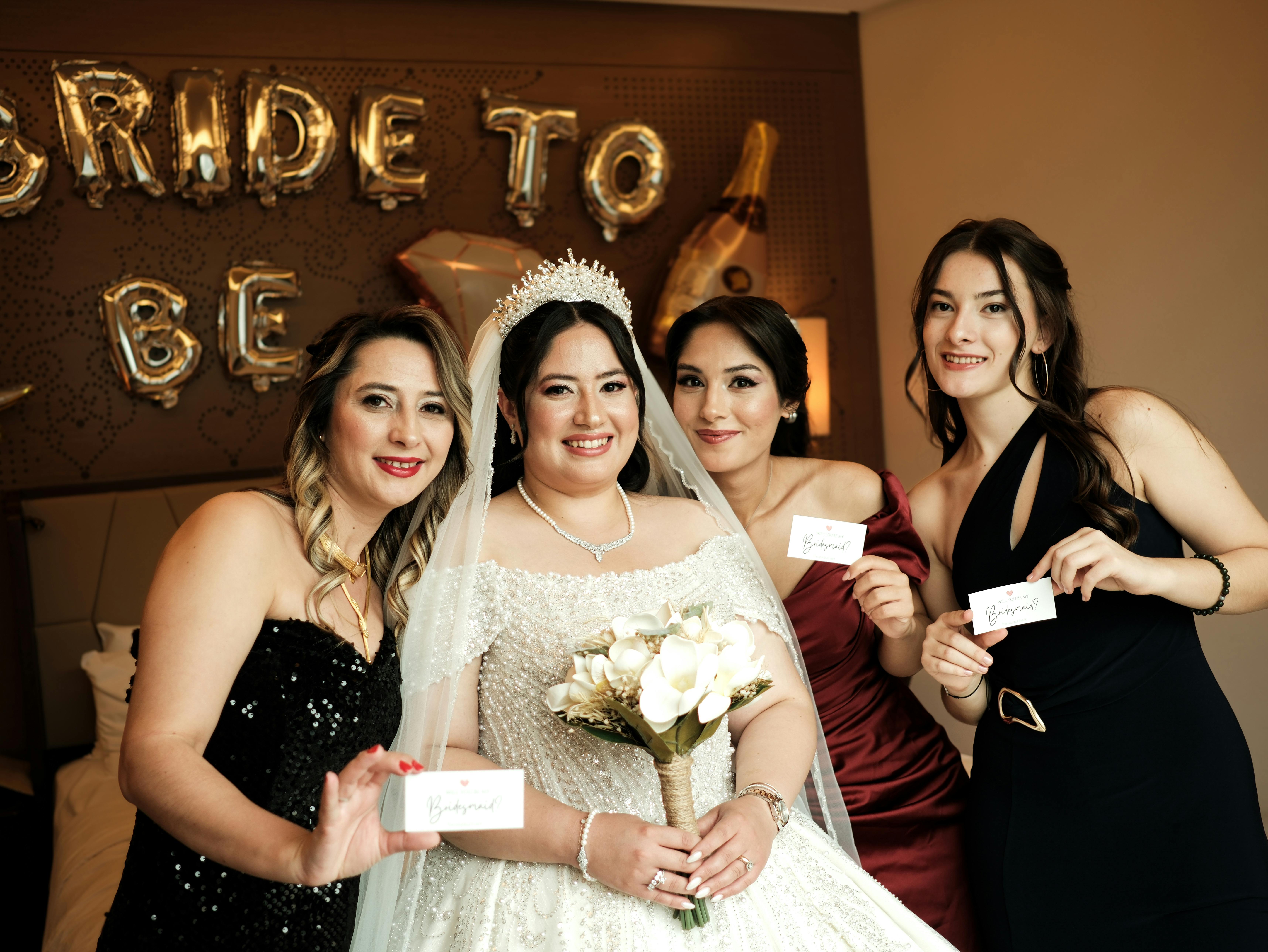 Joyful bride and bridesmaids posing together with bouquet indoors.