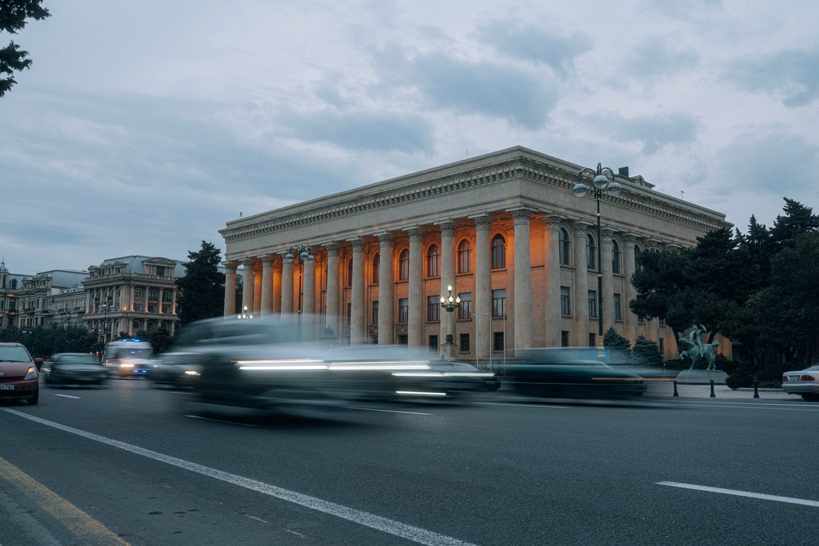 Cars streaking past a floodlit neoclassical civic hall at dusk — photo by Mahmut Yilmaz on Pexels