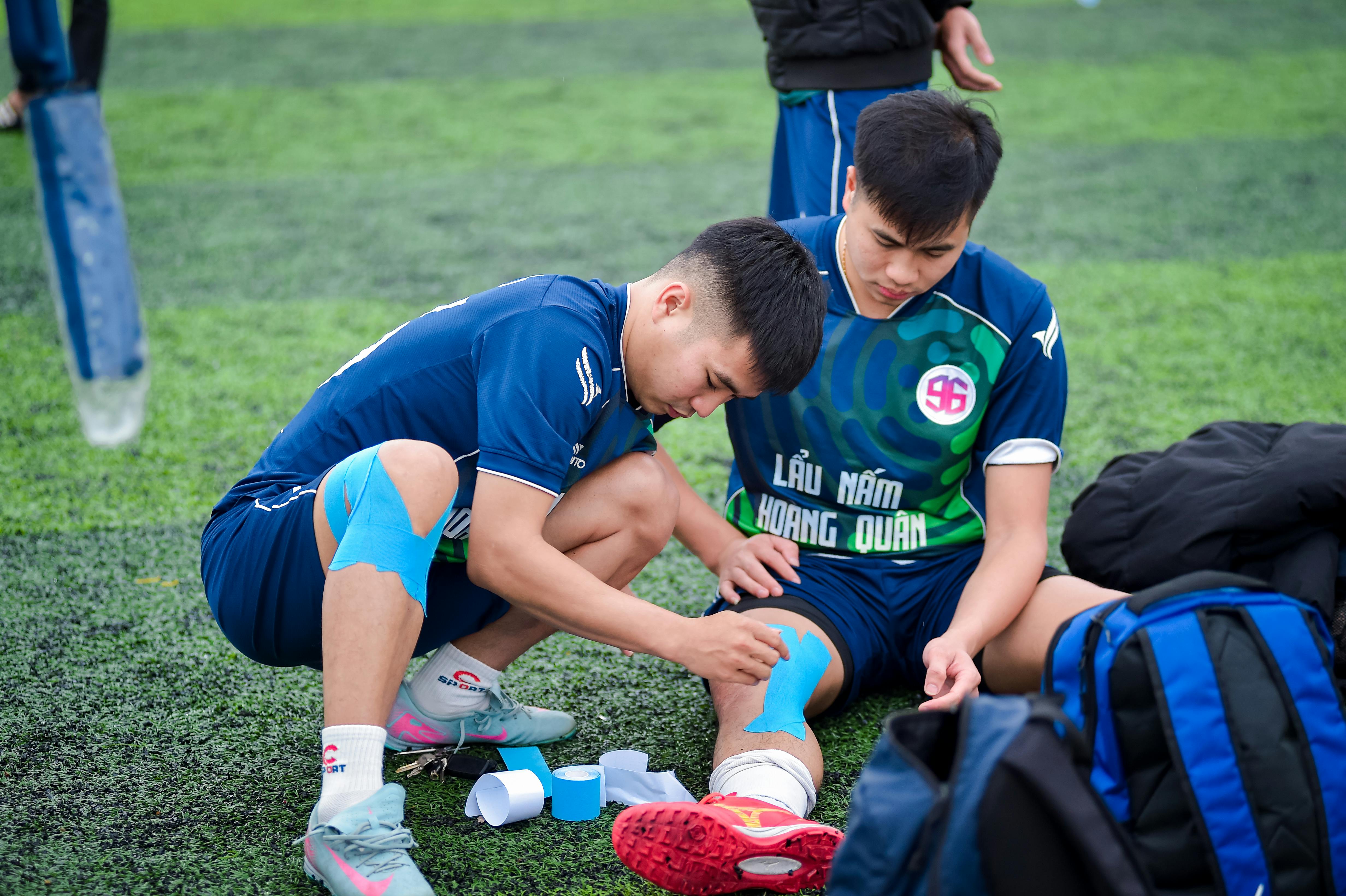 Football players applying kinesiology tape on the field in Hà Nội, Vietnam.