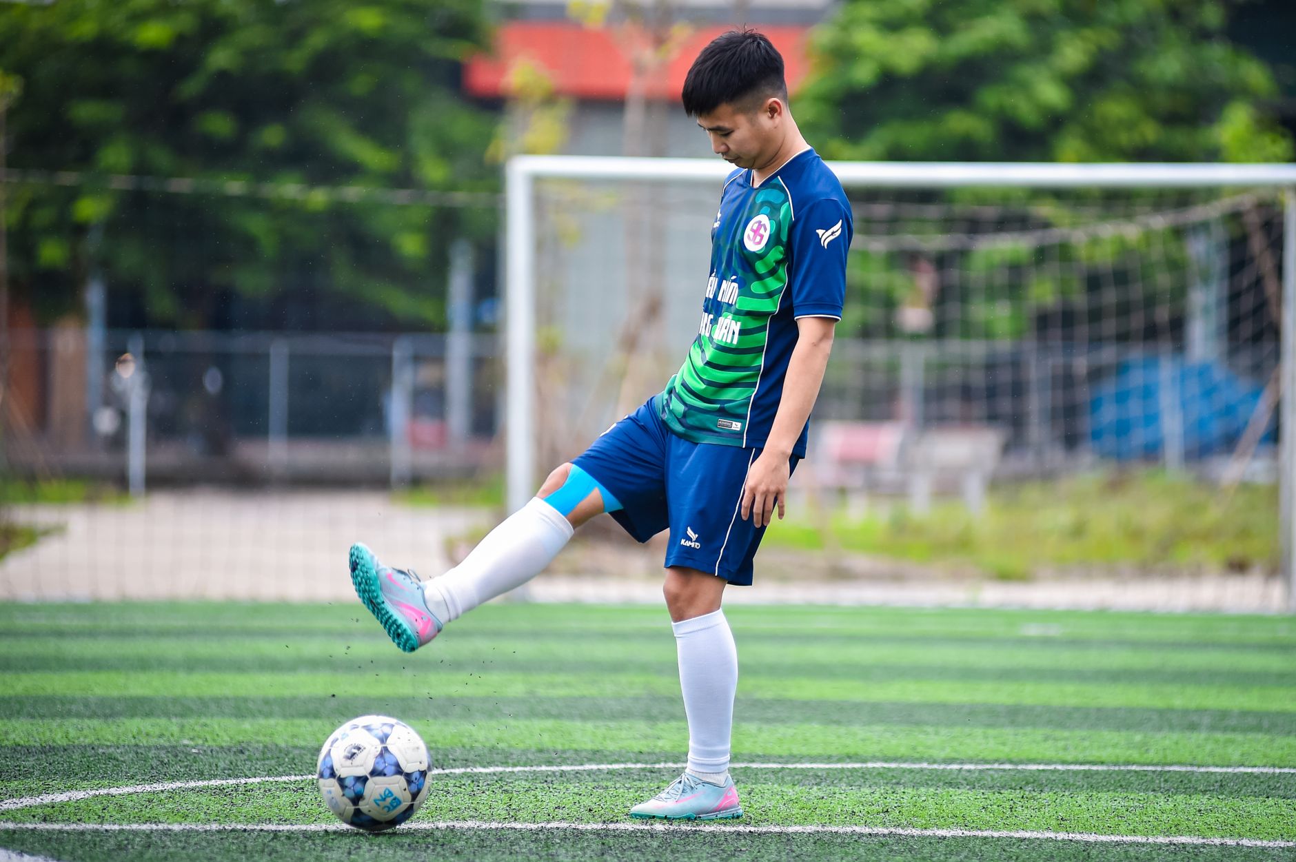 젖은 인조잔디 경기장에서 초보 축구선수가 새 축구화의 스터드와 발뒤꿈치 고정을 점검하는 장면