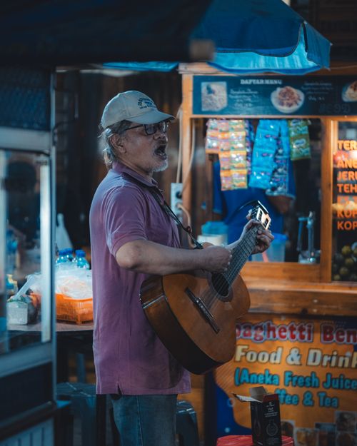 Free An elderly man playing guitar at a night market stall in Jakarta, Indonesia. Vibrant street ambiance. Stock Photo