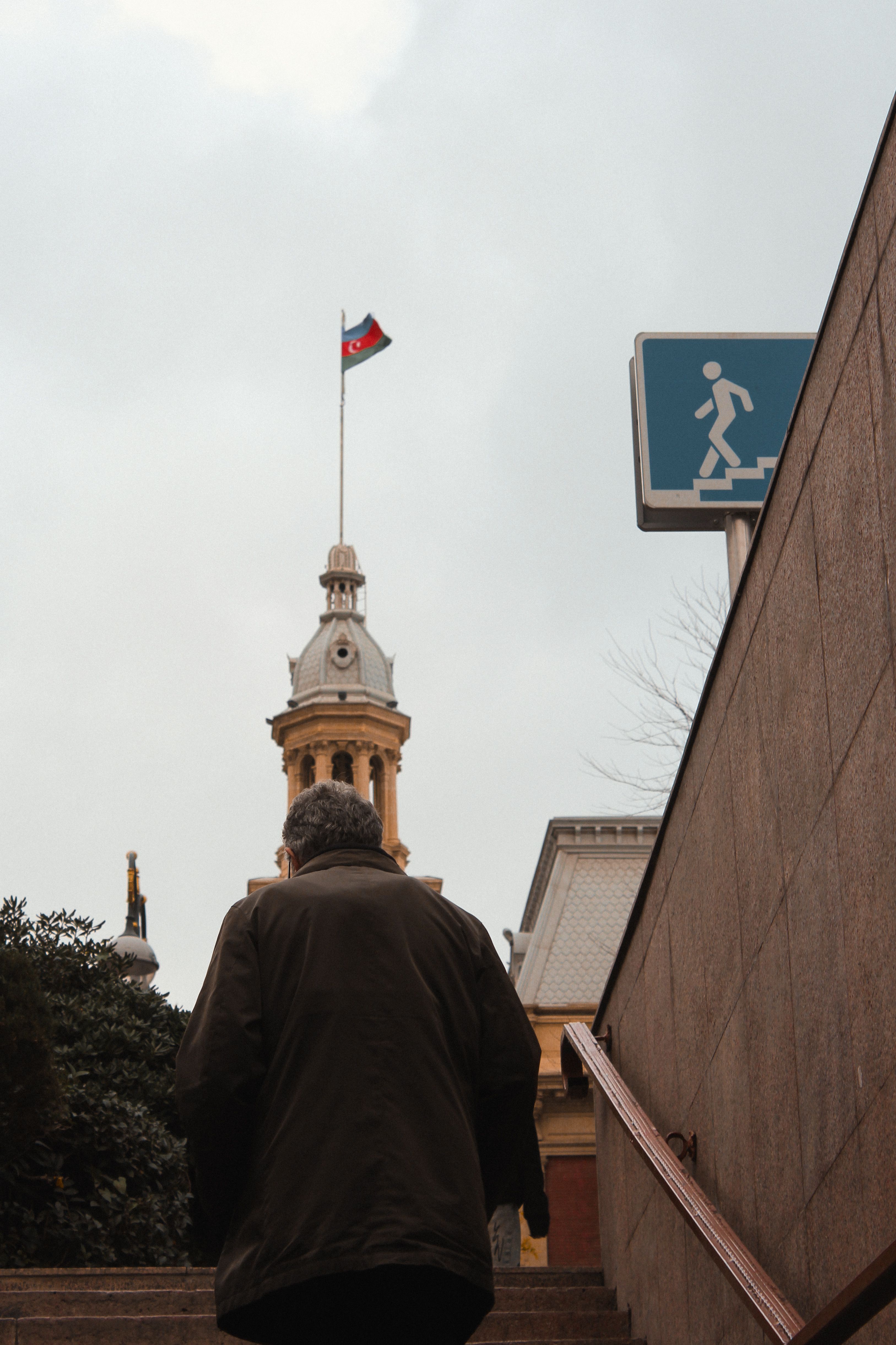 Man climbing stairs with historic clock tower and flag in background.