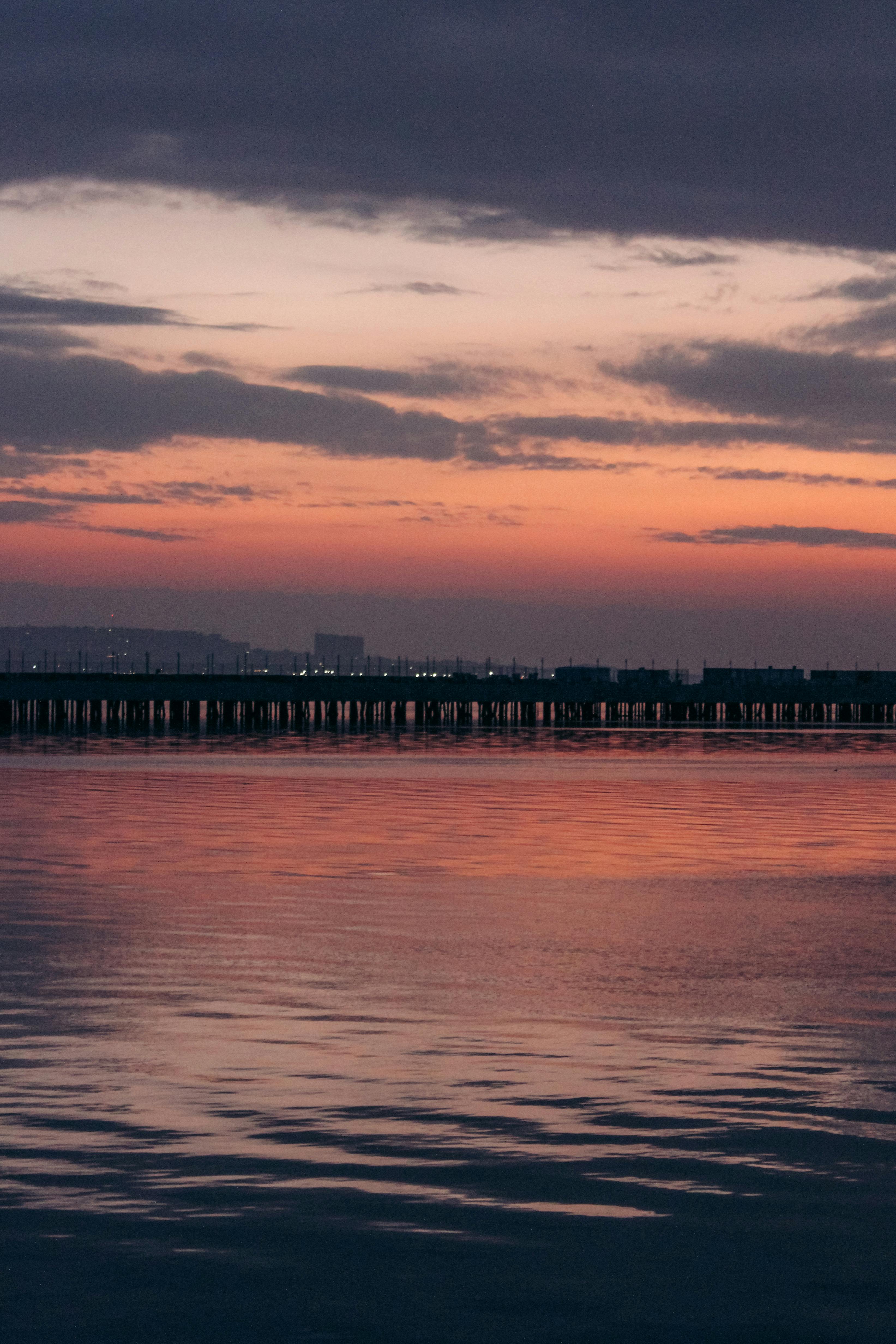 Serene sunset over a waterfront with a silhouette of a distant city skyline.