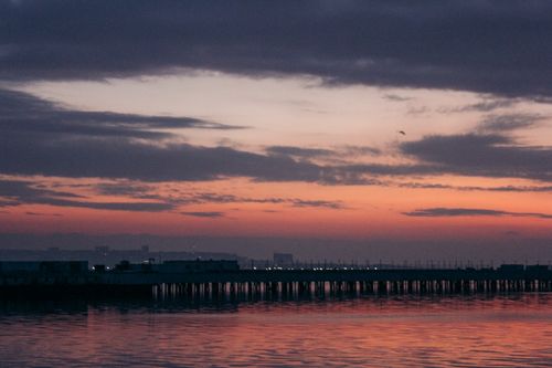 Free A tranquil view of a harbor at sunset with a pier silhouette against a colorful sky. Stock Photo