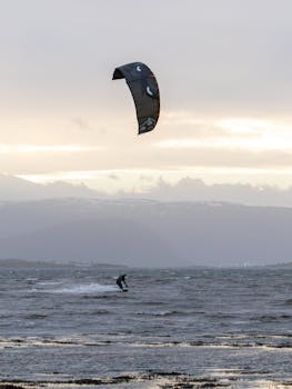 Dynamic shot of a kitesurfer on a windy day with mountains and clouds in the background.