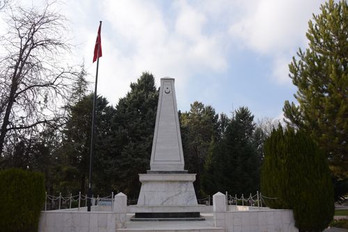 Free A tall stone obelisk monument in a park with surrounding trees and a national flag. Stock Photo