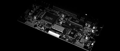 A high-contrast black and white photograph of a computer circuit board against a dark background.