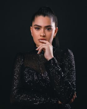 A woman in a sequin dress poses thoughtfully against a dark background.