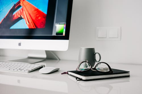 Imac Prateado Ativado Ao Lado Da Caneca De Cerâmica Cinza E óculos De Armação Preta