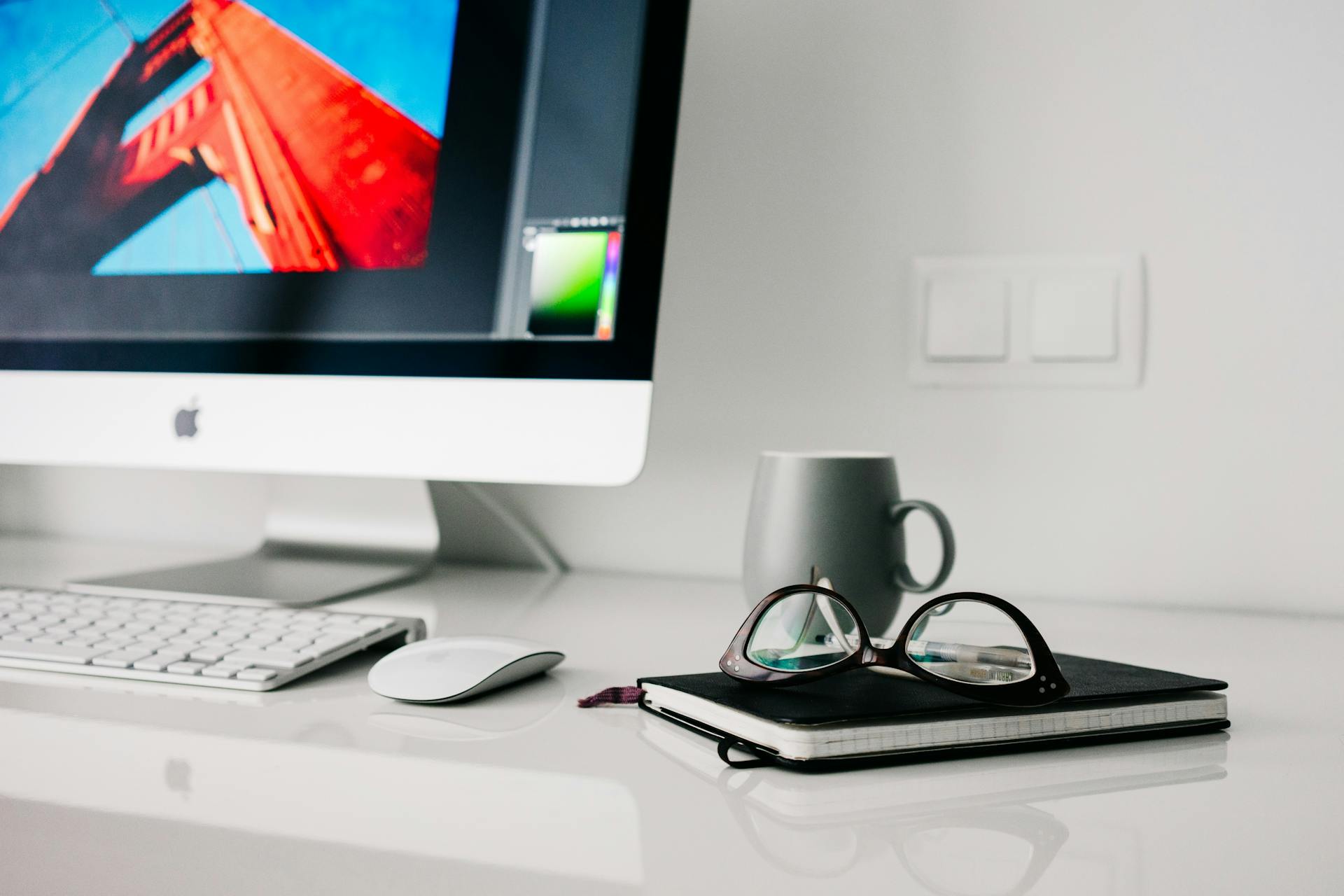 Stylish office workspace featuring a desktop computer, glasses, and notebook.