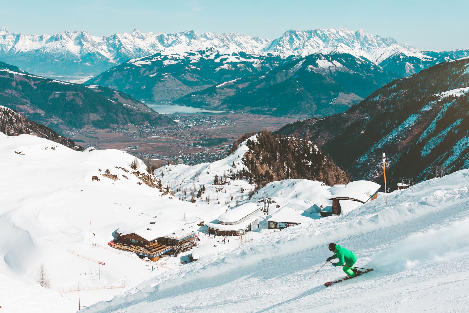 Skier carving down a groomed slope with mountains in the background