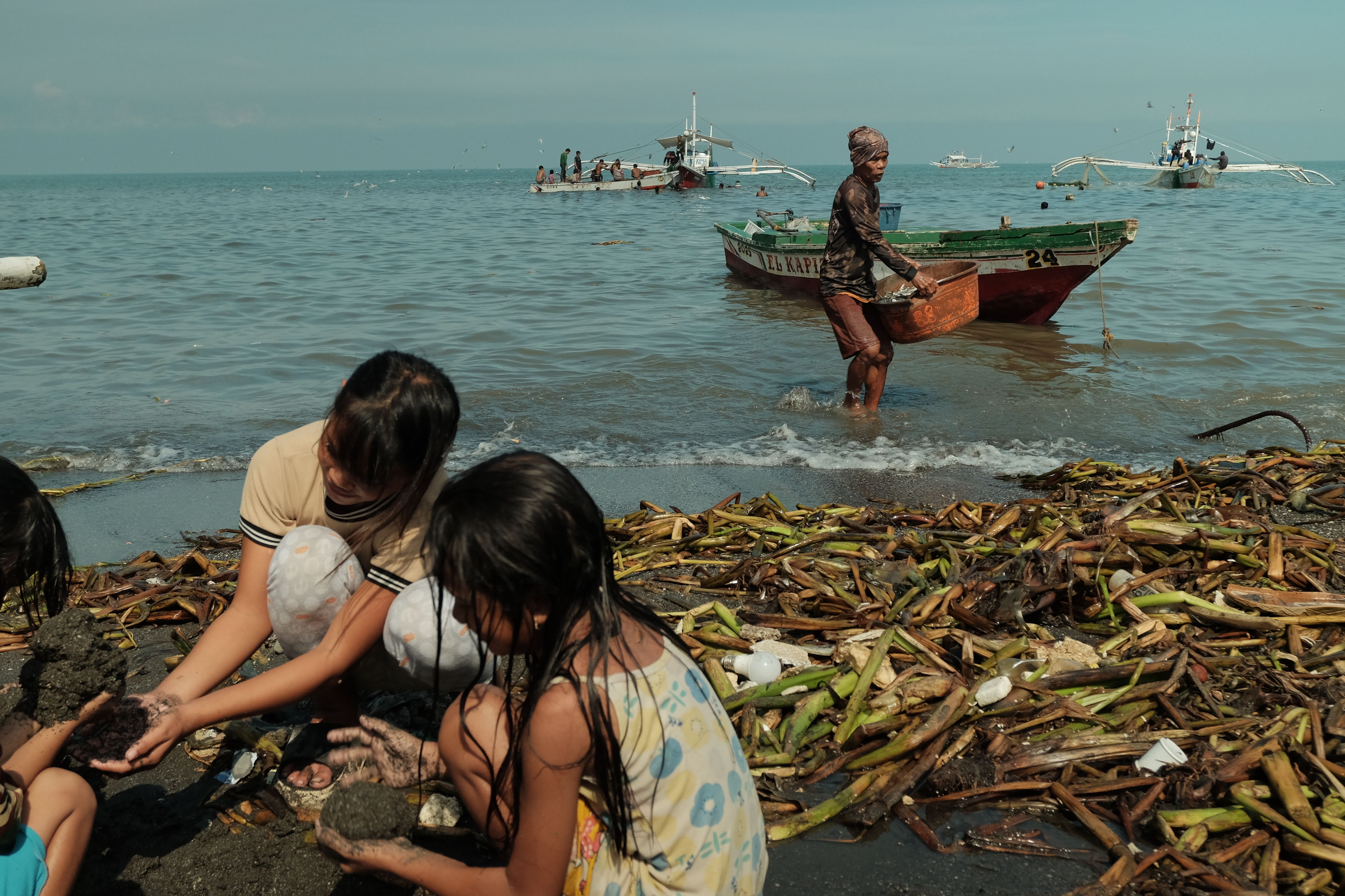 Children playing on the beach while fishermen work in boats in the Philippines.