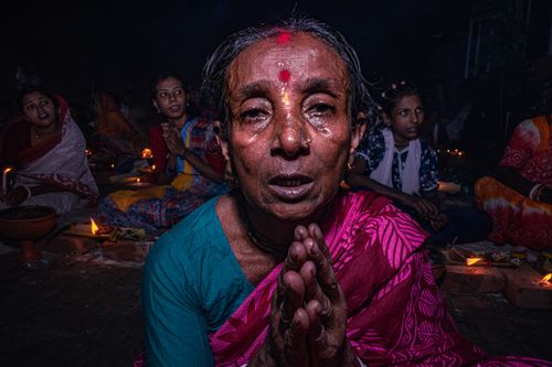 Free An elderly woman in traditional attire praying during a vibrant cultural ceremony with candles. Stock Photo