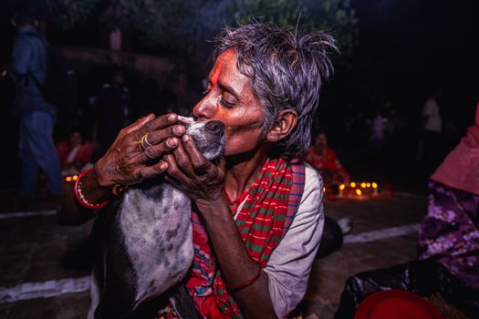 An elderly woman lovingly embraces her dog at a nighttime gathering with lit candles.