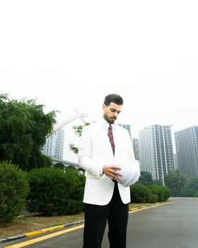 Male architect in white suit examining plans outdoors in modern cityscape