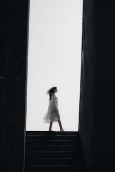 Dramatic silhouette of a woman in a white dress walking between walls in Armenia.