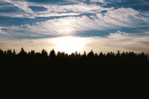 A stunning sunrise over a forest silhouette with dramatic cloud formations.